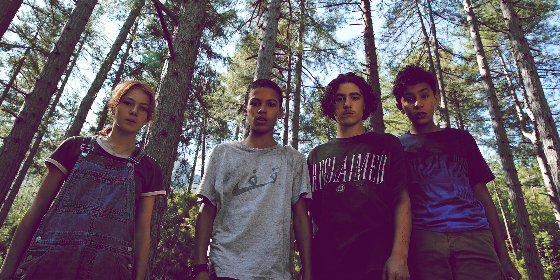 Trzech nastoletnich chłopców i jedna dziewczynka stoją na tle lasu. Patrzą na wprost.